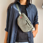 Model trägt olivgrüne Bauchtasche mit einem Himbeer-Icon darauf gestickt. Die Bauchtasche wird über die Schulter getragen.