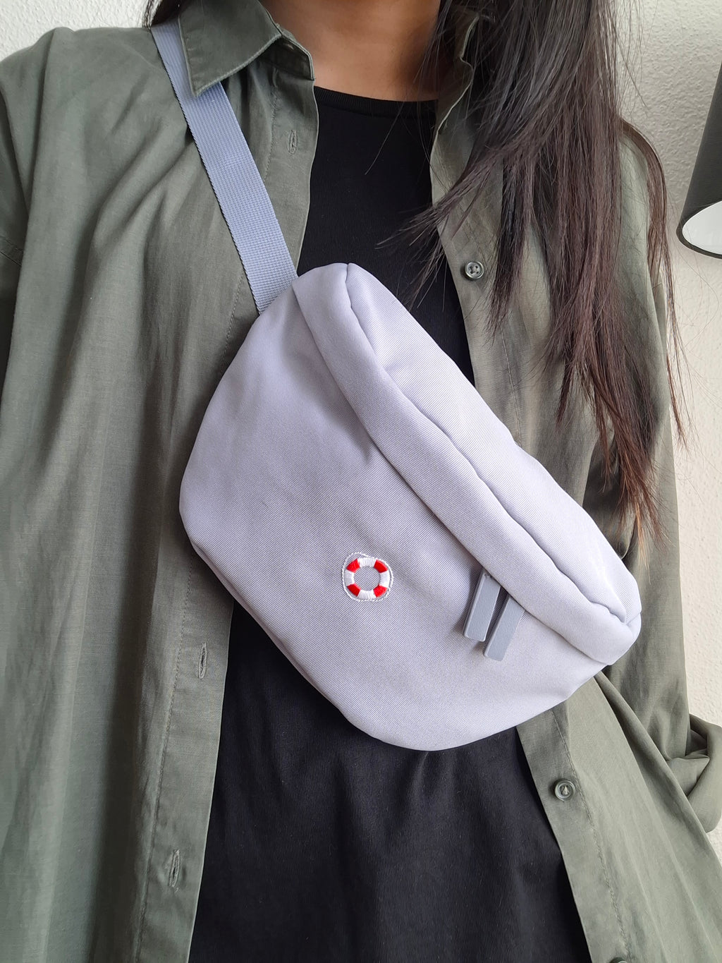 Blau-graue Bauchtasche mit einem Rettungsring-Icon darauf gestickt.