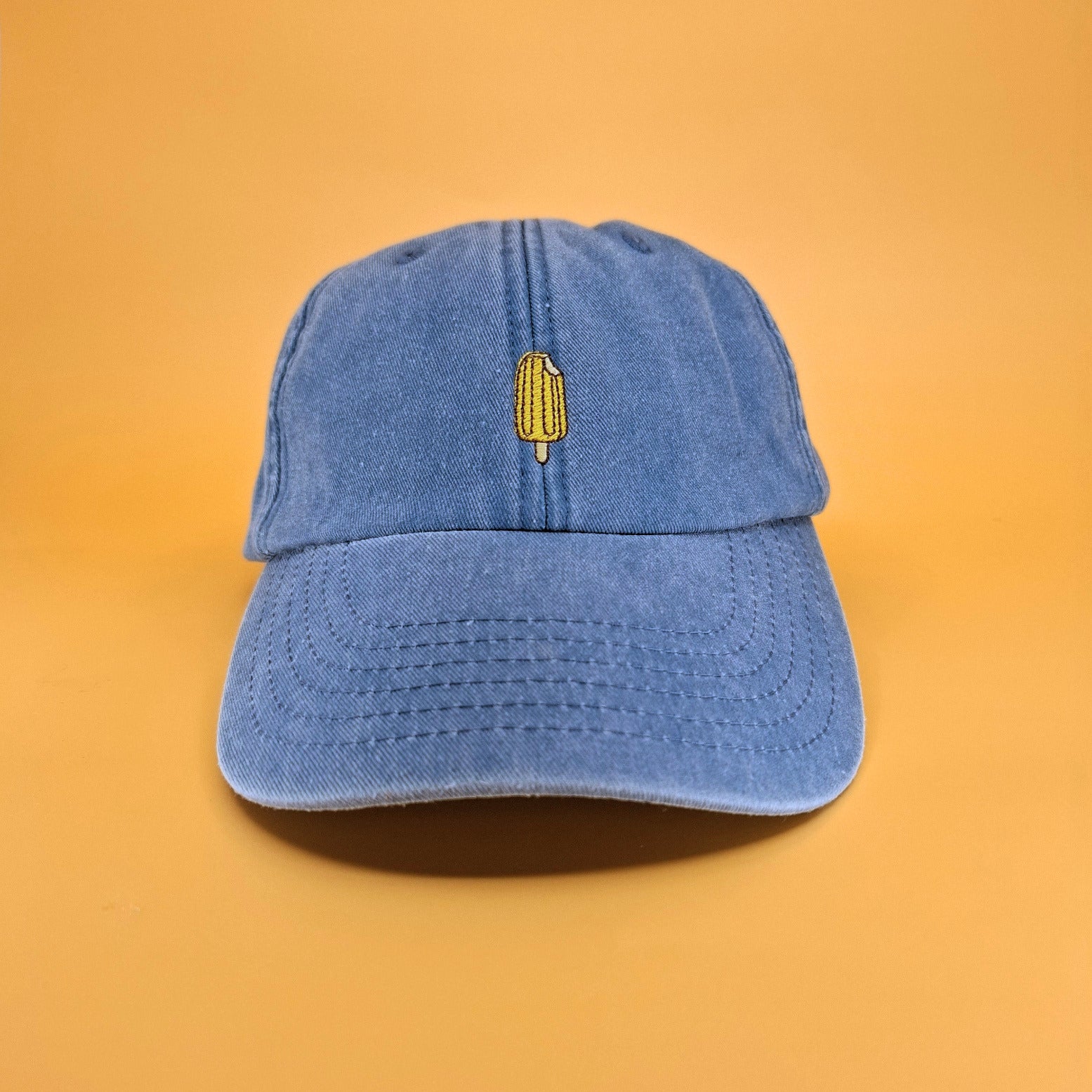 Blaue Cap mit einem gelb-orangen Eis am Stiel darauf gestickt