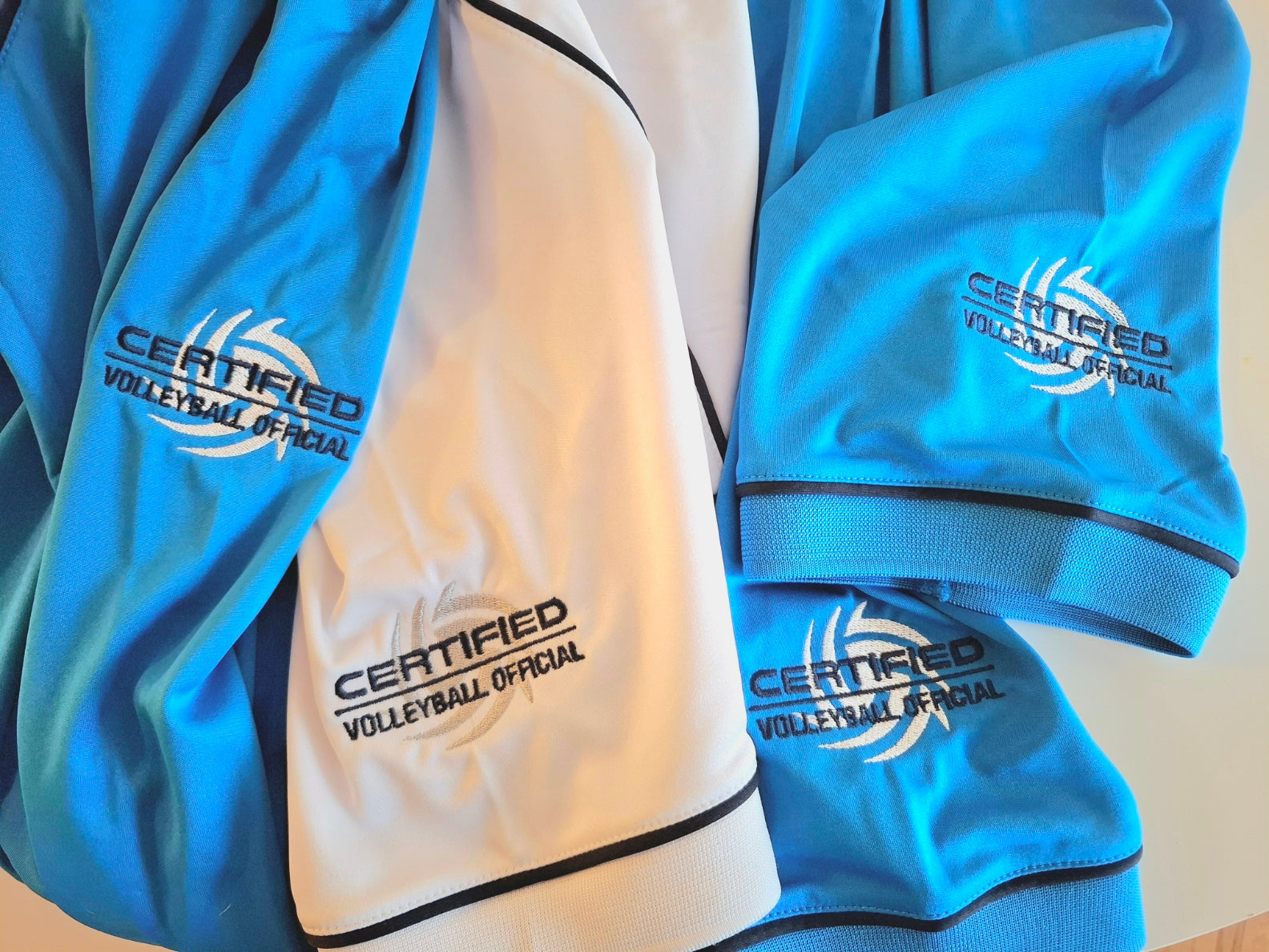 Nahaufnahme von Ärmeln von Sport-Tshirts gestickt mit einem Logo für "Certified Volleyball Official"