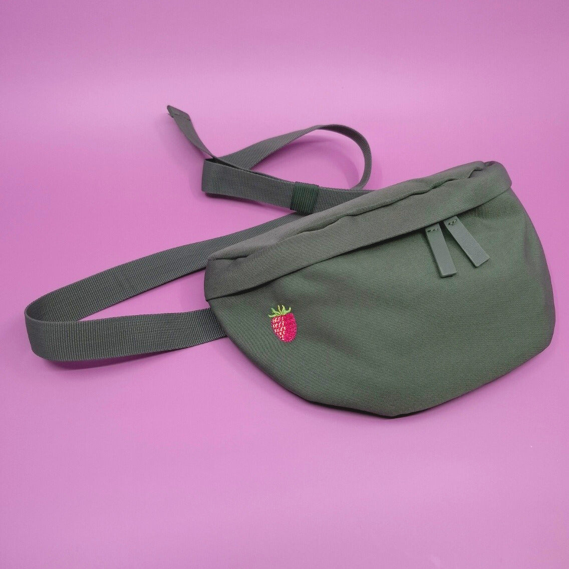 Olivgrüne Bauchtasche mit einem Himbeer-Icon gestickt auf der linken Seite.
