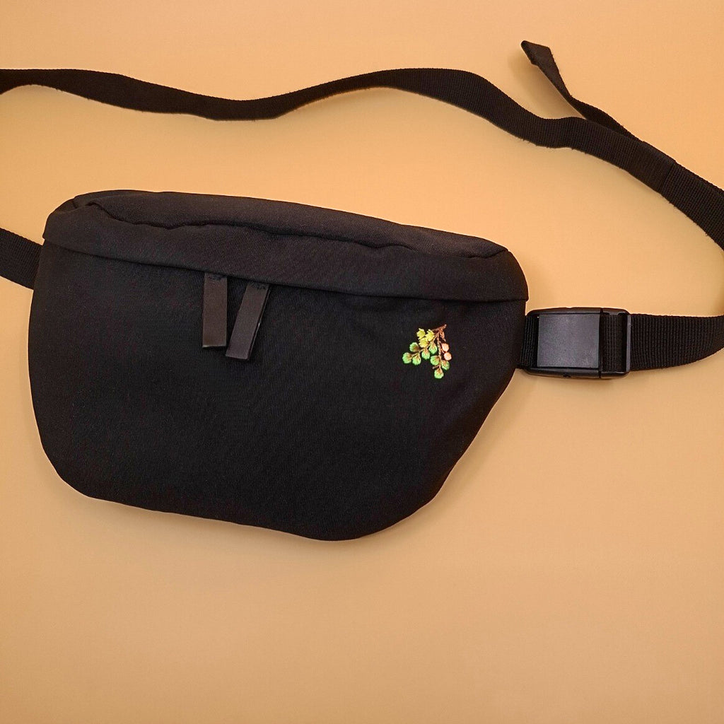 Schwarze Bauchtasche mit einem kleinen Zweig-Motiv gestickt auf der rechten Seite.