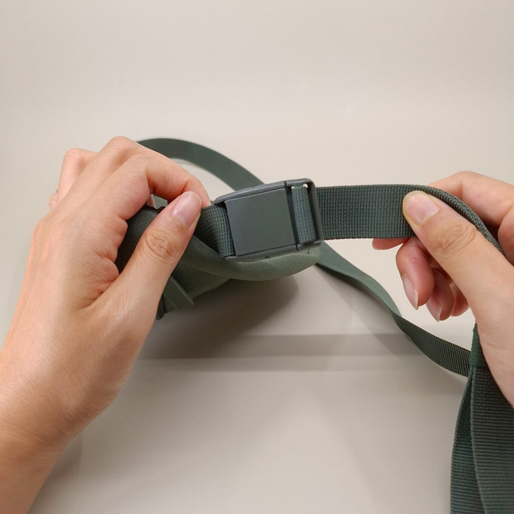 Nahaufnahme der Verschlussschnalle einer olivgrünen Bauchtasche. Die Schnalle ist aus Kunststoff.