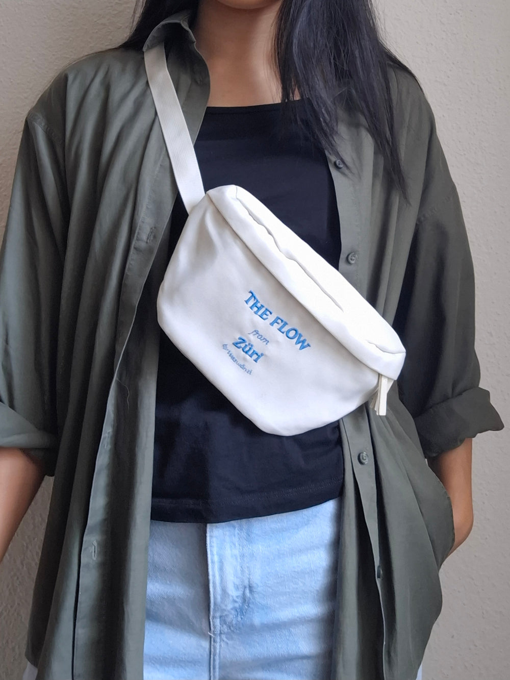 Person trägt eine weisse Bauchtasche bestickt mit einem Logo in blau "The Flow from Züri"