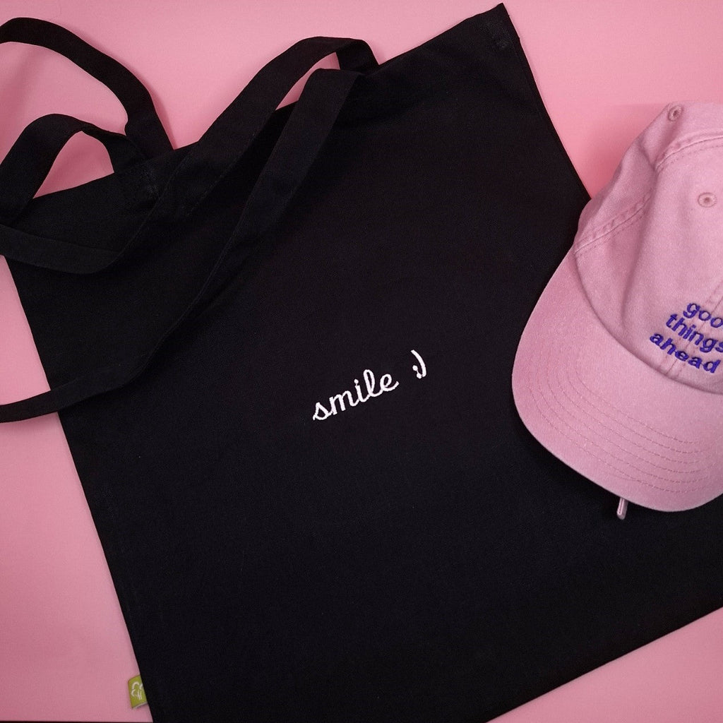 Schwarze Stofftasche bestickt mit dem Text "smile :)" in weiss und in einer Script-Schrift