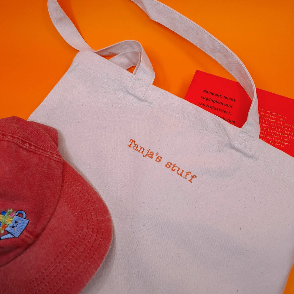 Beige Stofftasche mit dem Text "Tanja's stuff" darauf gestickt in orange und einer Serifen-Schrift