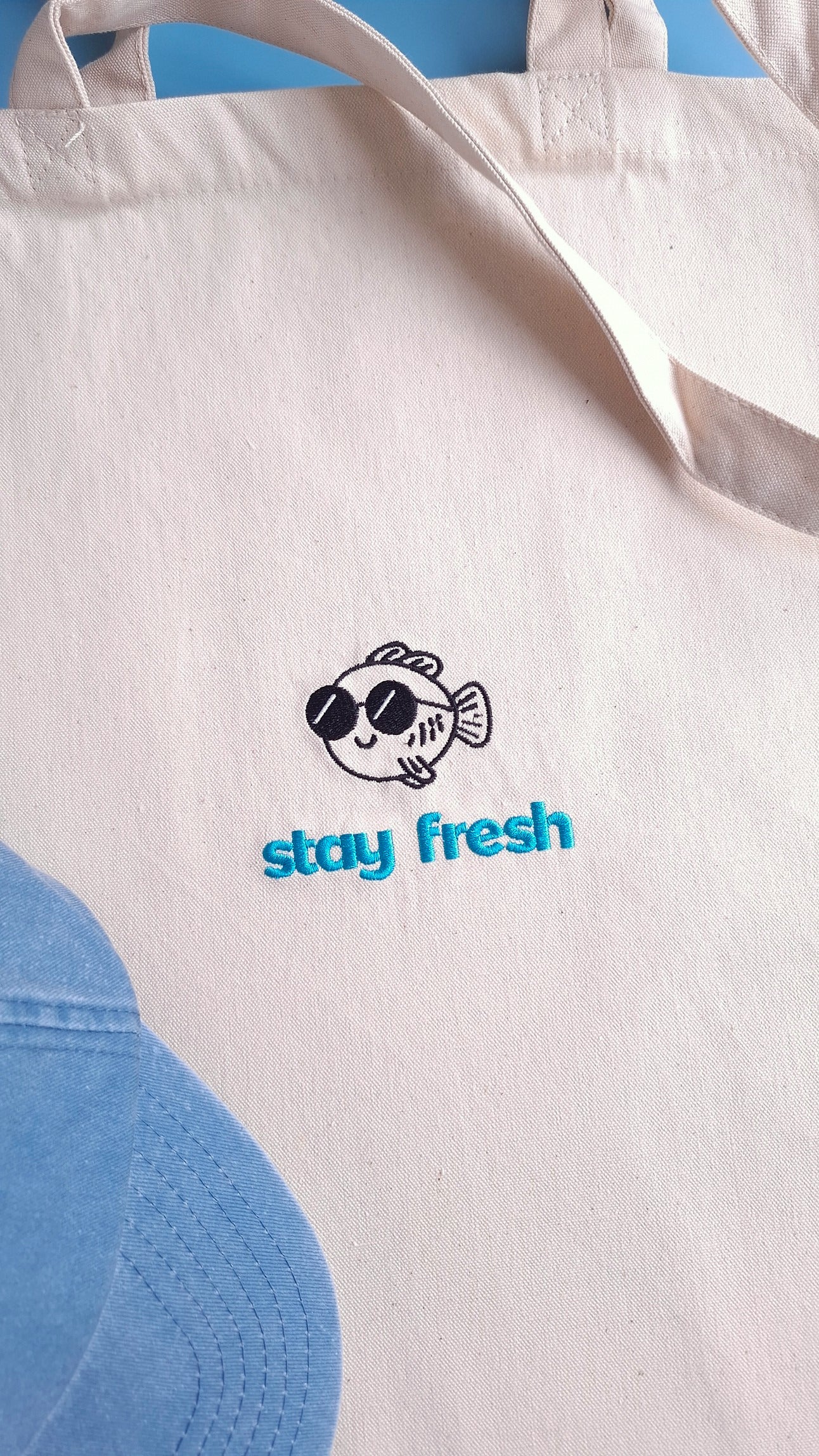Beige Stofftasche bestickt mit einem Fisch im Comic-Stil und dem Text "stay fresh" in blau darunter