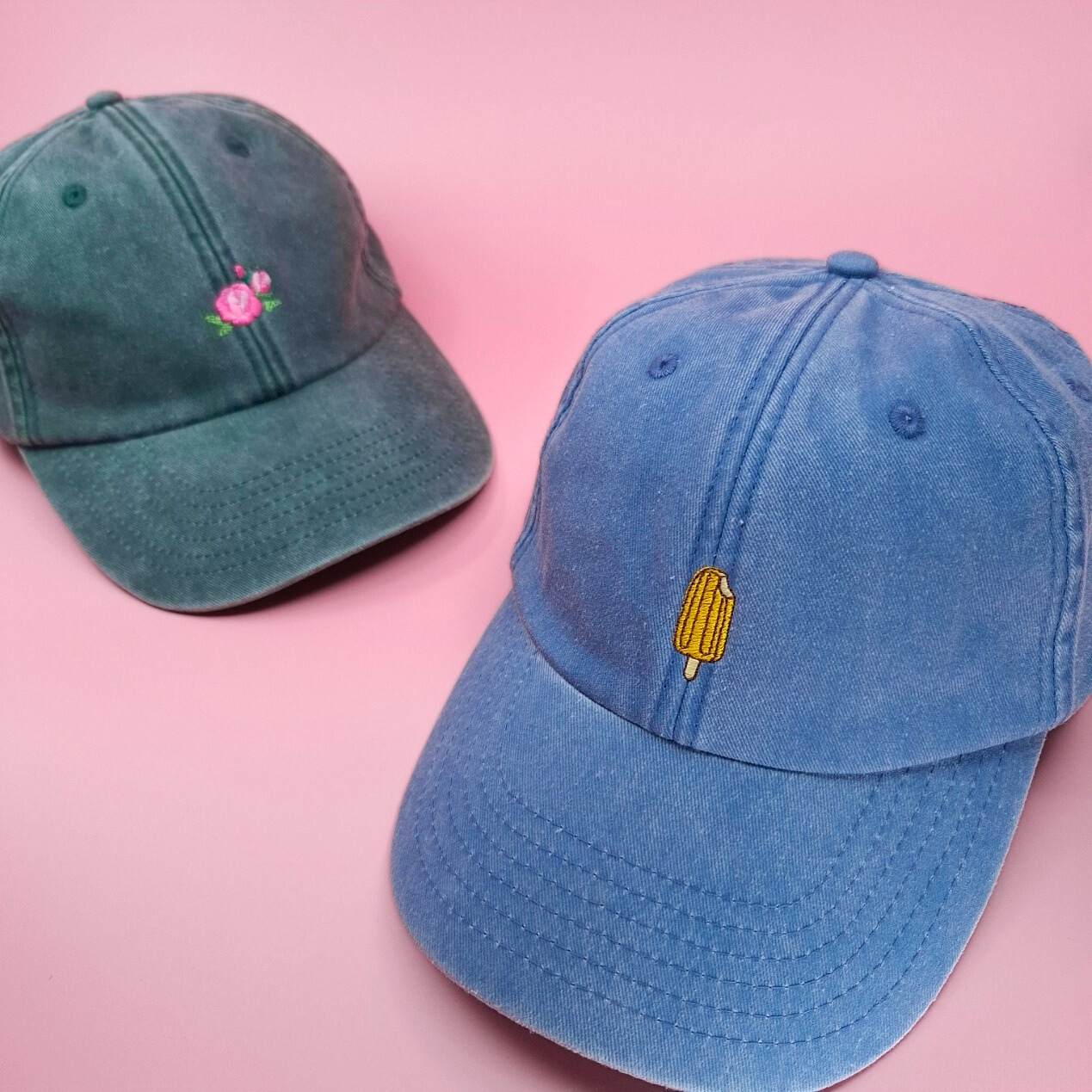 Eine dunkelgrüne Cap mit einem Rosen-Icon und eine blaue Cap mit einem Wassereis-Icon