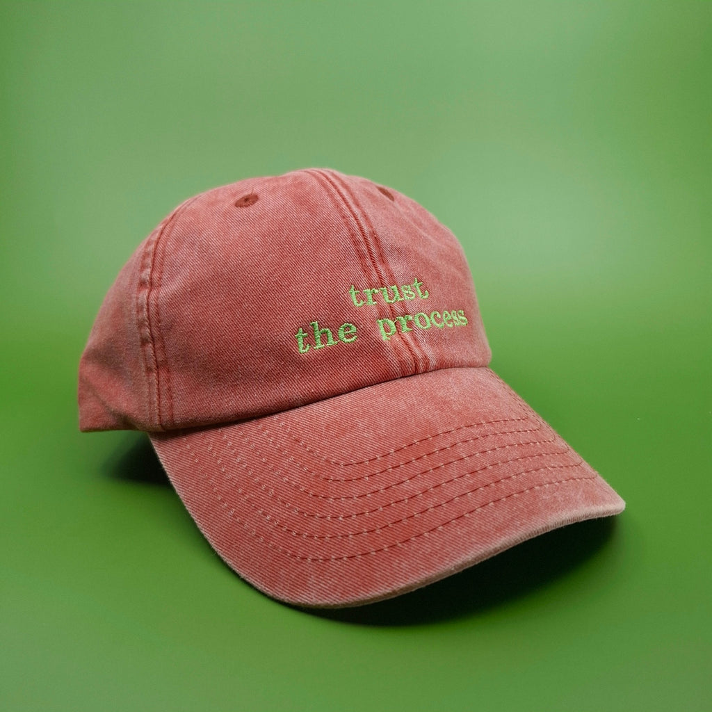 Orange Cap mit besticktem Text "trust the process" in leuchtendem grün.
