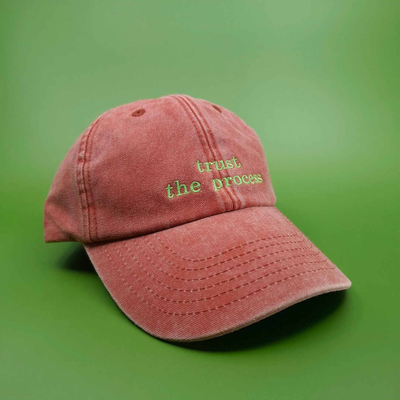 Orange Cap mit besticktem Text "trust the process" in leuchtendem grün.