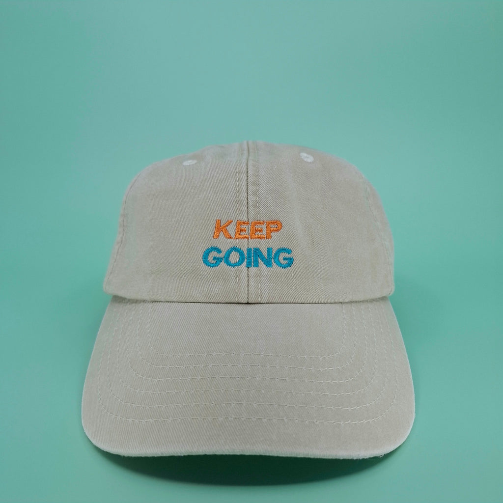 Beige Cap mit besticktem zweifarbigen Schriftzug "keep going" in orange und cyan.