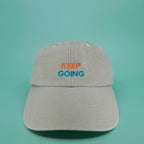 Beige Cap mit besticktem zweifarbigen Schriftzug "keep going" in orange und cyan.