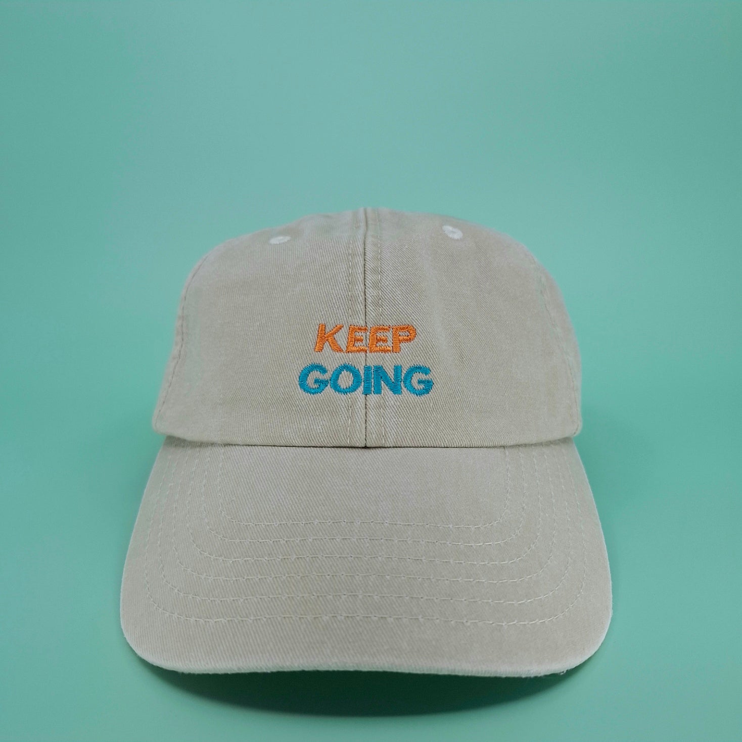 Beige Cap mit besticktem zweifarbigen Schriftzug "keep going" in orange und cyan.