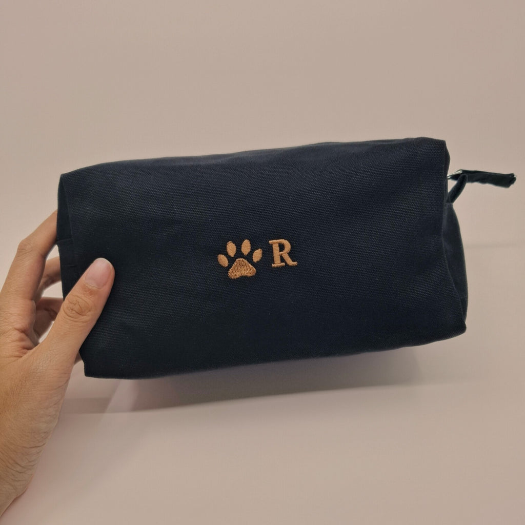 Schwarze Kosmetiktasche mit einem Pfoten-Icon und einem "R" darauf gestickt in braun.