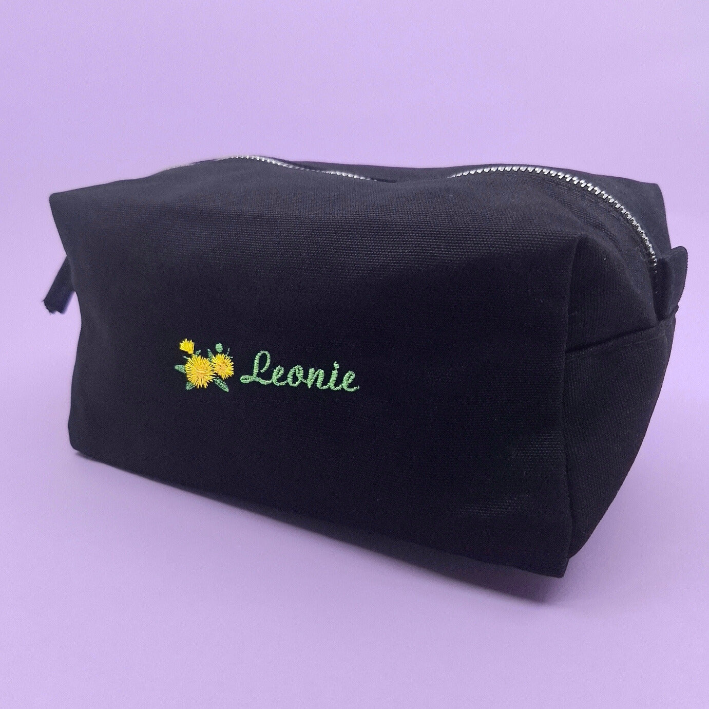 Schwarze Kosmetiktasche mit einem Löwenzahn-Icon und dem Namen "Leonie" darauf gestickt.