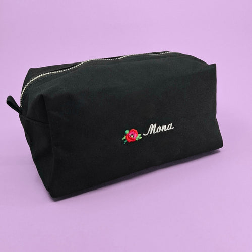 Schwarze Kosmetiktasche mit einem Mohnblumen-Icon und dem Namen "Mona" bestickt.