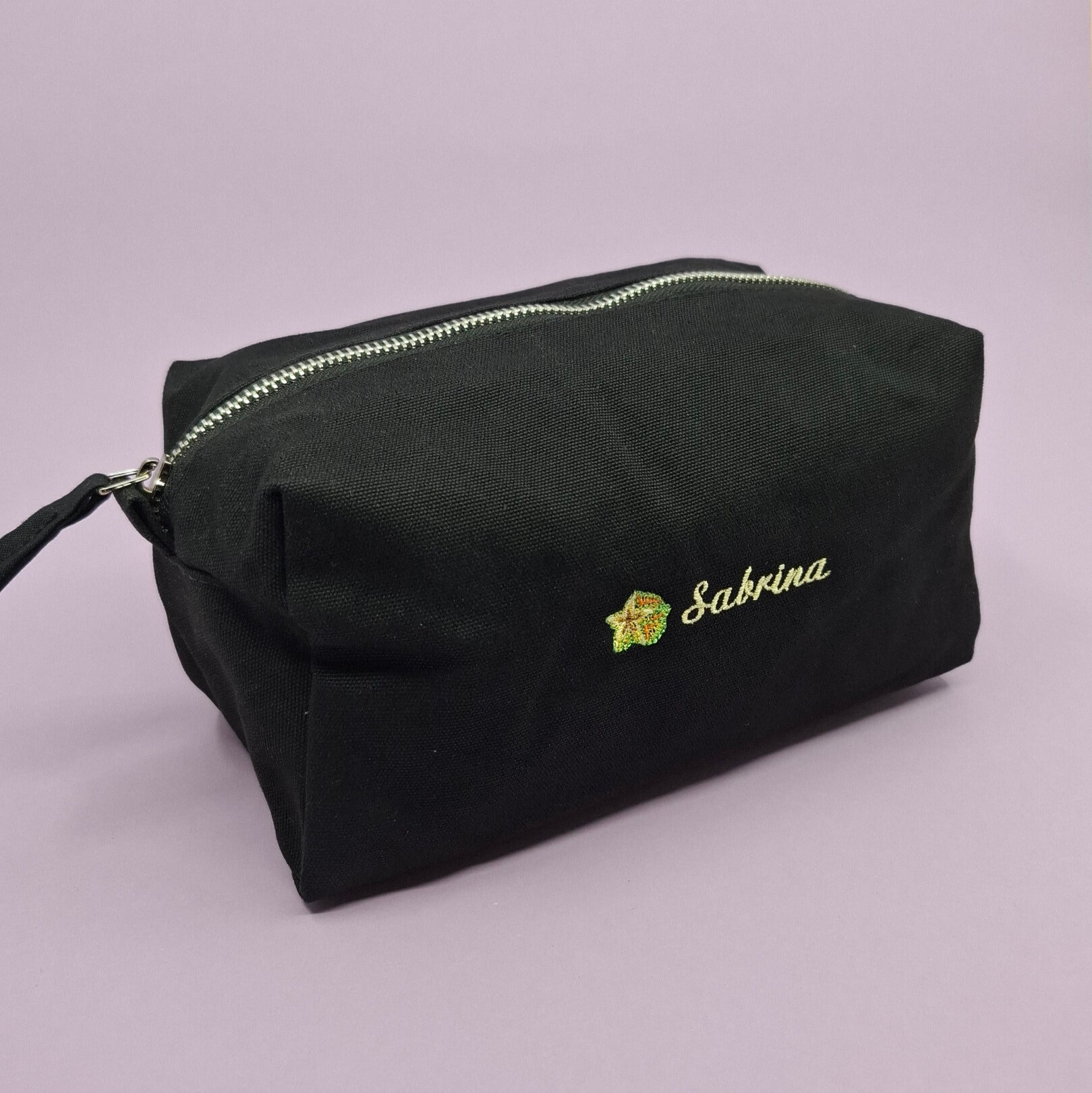 Schwarze Kosmetiktasche mit einem Sternfrucht-Icon und dem Namen "Sabrina" darauf gestickt.